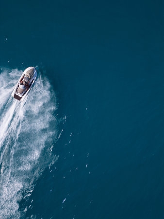 Aerial view of a jet ski speeding across dark blue water, leaving a dynamic white trail. Captured by...
