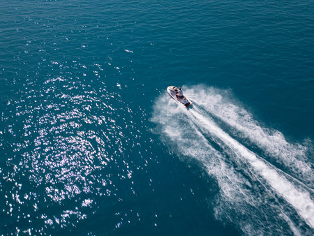 Aerial view of a jet ski speeding across dark blue water, leaving a dynamic white trail. Captured by drone from above, showcasing motion, power, and summer fun on the seaの写真素材