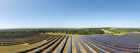 Aerial view of a large solar power plant with rows of photovoltaic panels installed on open land, generating clean renewable energy under a clear skyの写真素材