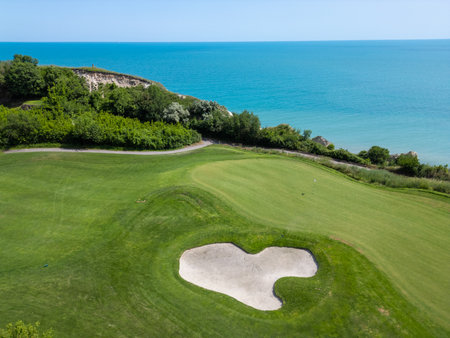 Scenic aerial view of a coastal golf course with green fairways, sand bunkers, golf carts, and players, surrounded by lush vegetation and turquoise seaの写真素材