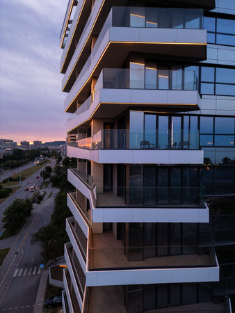 Modern residential building with glass balconies and LED lighting at sunset. Urban architecture and city living concept with soft sky reflections and evening ambianceの写真素材