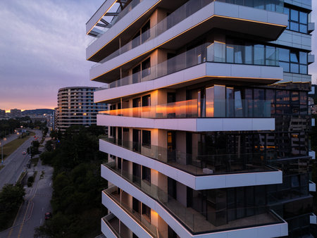 Modern residential building with glass balconies and LED lighting at sunset. Urban architecture and city living concept with soft sky reflections and evening ambianceの写真素材