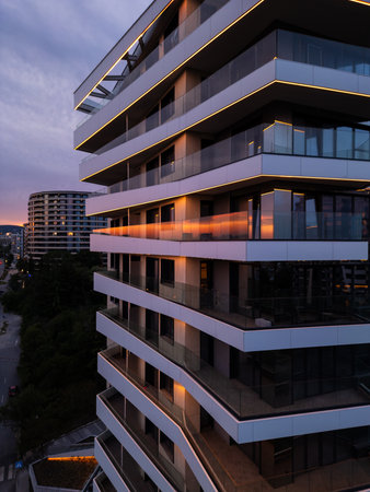 Modern residential building with glass balconies and LED lighting at sunset. Urban architecture and city living concept with soft sky reflections and evening ambianceの写真素材