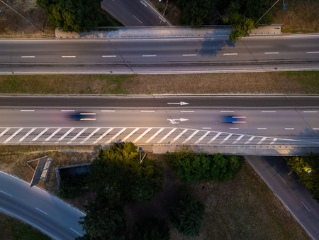 Aerial view of multilane highway with fast-moving cars at twilight. Motion blur emphasizes speed. Urban infrastructure with directional arrows, trees, and intersecting roadsの写真素材