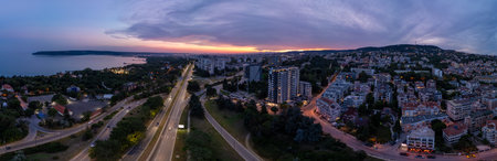 Aerial panoramic view of Varna, Bulgaria at sunset. Urban landscape with coastal city lights, residential buildings, highways, and dramatic sky over the Black Seaの写真素材