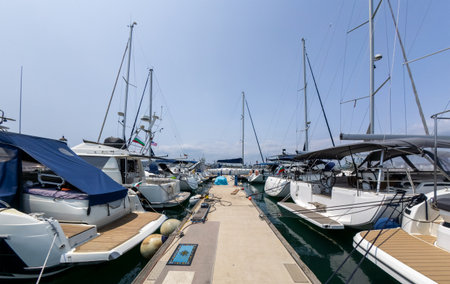 Marina with moored yachts and sailboats on a sunny day. Walkway between boats leads into the...