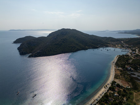 Aerial view of a peaceful bay with anchored sailboats and lush green hills. The calm sea reflects the sunlight, creating a serene and scenic coastal landscapeの写真素材