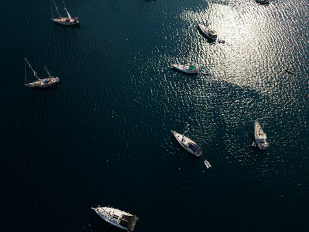 Aerial top-down view of several sailboats anchored in calm dark blue sea water with sun reflections. Peaceful summer maritime scene ideal for travel and vacation themesの写真素材