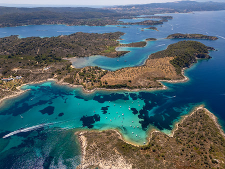 Aerial view of a stunning turquoise bay filled with anchored boats near a scenic Mediterranean coastline with olive groves and clear water, captured on a bright summer dayの写真素材