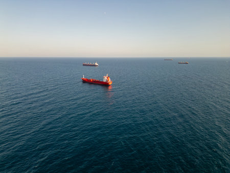 Aerial video of cargo ships anchored in calm open sea under clear sky. Peaceful maritime scene showcasing global trade and ocean transportation at sunrise or sunsetの写真素材