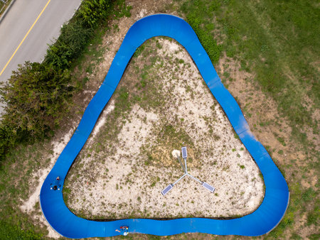 Aerial view of blue pump track with two kids riding scooters, top down perspective of outdoor sports activity, curved ramps and recreational parkの写真素材