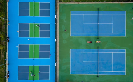 Aerial view of adjacent tennis and pickleball courts with players practicing on bright blue and green surfaces, showcasing a vibrant sports complex from aboveの写真素材