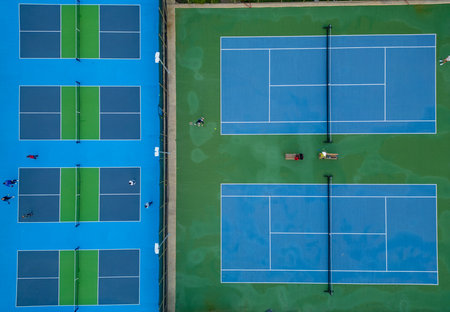 Aerial view of adjacent tennis and pickleball courts with players practicing on bright blue and green surfaces, showcasing a vibrant sports complex from aboveの写真素材