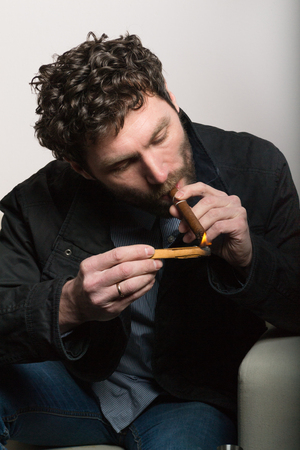 bearded man sitting on a chair and smoking a cigar