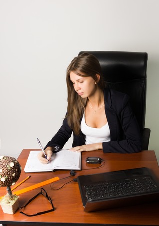 business woman in a suit sitting at a desk. on the table laptop and notebook.の写真素材