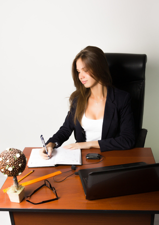 business woman in a suit sitting at a desk. on the table laptop and notebook.の写真素材