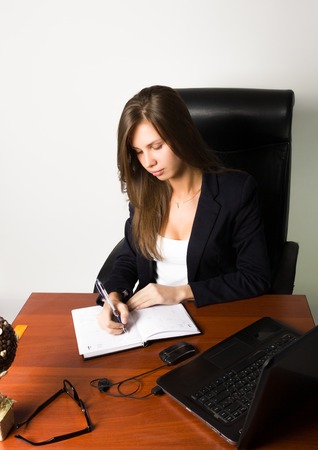business woman in a suit sitting at a desk. on the table laptop and notebook.の写真素材