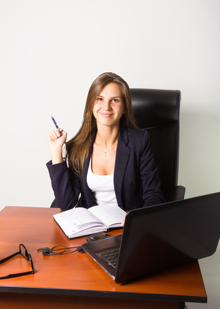 Pretty woman in a business suit sitting at a desk with computer. Studio shot.の写真素材
