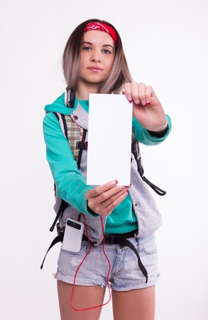 Young brunette female student standing and listening to music from your device. Beautiful young backpacker. Young female student holding a white sheetの写真素材