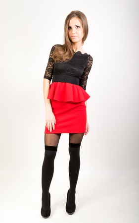Beautiful sexy brunette girl in the studio on a gray background in a red short skirt and stockingsの写真素材