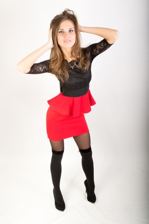 Beautiful sexy brunette girl in the studio on a gray background in a red short skirt and stockingsの写真素材