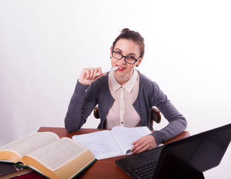 Young beautiful female teacher sitting at the table and reads the book and makes notes in a notebookの写真素材