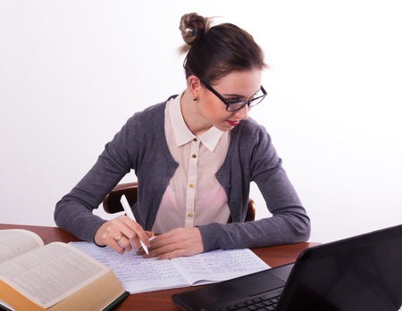 Young beautiful female teacher sitting at the table and reads the book and makes notes in a notebookの写真素材