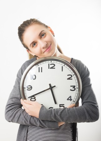Beautiful young woman looking at a large silver retro clock that she is holding, she is wonders how much time passedの写真素材