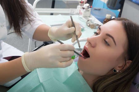 Young woman visiting dentist in stomatological clinic. Doctor examines the oral cavity on tooth...