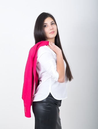 A young pretty slim asian woman standing in a leather skirt and white blouse. holding a red jacket on shoulderl.の写真素材