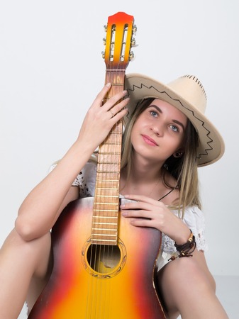 beautiful young leggy blond Country girl in a litl white dress and cowboy hat with a guitar.