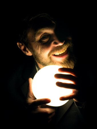 bearded man in the dark, holding in front of a lamp, expresses different emotions.の写真素材