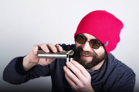 Fashion hipster cool man in sunglasses and colorful clothes pours himself a drink from a metal flask.の写真素材