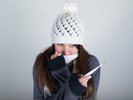 young woman in a knitted hat and scarf, holding hands in the thermometer. she seems sick.の写真素材