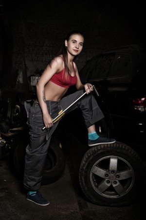 sexy girl mechanic sitting on a tire holding a wrench in his hand. colorless life concept.の写真素材