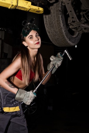 Beautiful young female mechanic inspecting car in auto repair shop. girl mechanic in overalls changes a wheel on a car in garage. Sexy mechanic.の写真素材