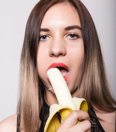 Young amazed woman in lacy lingerie holding a banana, she is going to eat a banana. she sucks a banana.の写真素材