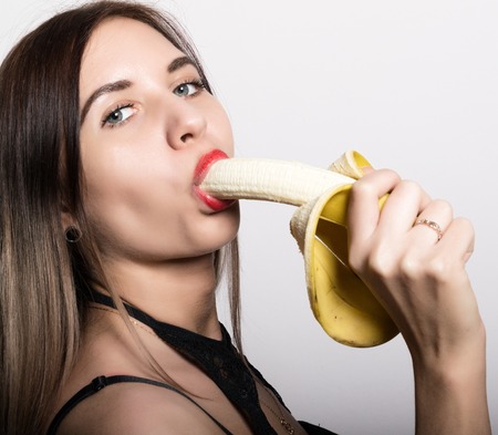 Young amazed woman in lacy lingerie holding a banana, she is going to eat a banana. she sucks a banana.の写真素材