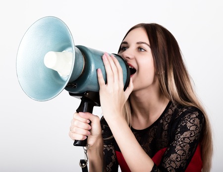 close-up portrait of a beautiful girl in a red dress with lace sleeves, she yells into a bullhorn. Public Relations.の写真素材