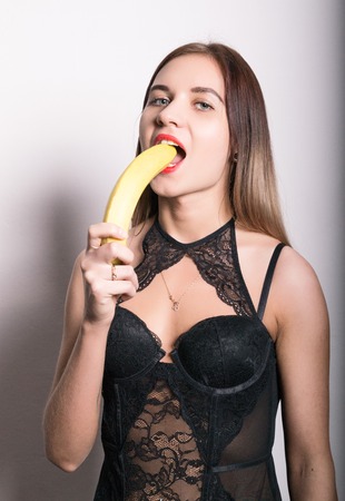 Young amazed woman in lacy lingerie holding a banana, she is going to eat a banana.の写真素材