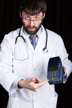 close-up portrait of a medical doctor, he proposes to pay for treatment in pos-terminal. concept of high cost of the treatment.の写真素材