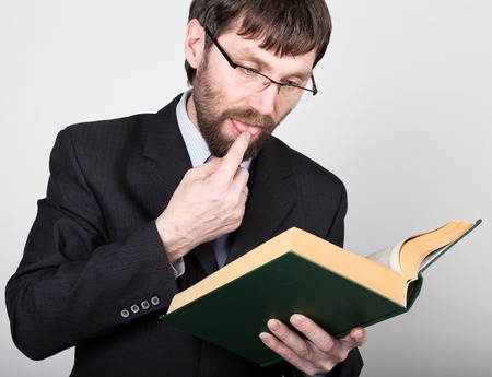 bearded businessman in a business suit and tie, reading a thick book.の写真素材