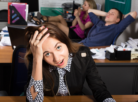 beautiful office female worker in panic holding his head. on a background sleeping colleagues. office concept.の写真素材