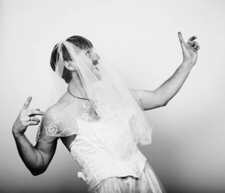 bearded man in a woman's wedding dress on her naked body, holding a flower. on his head a wreath of flowers. funny bearded bride, black and white.の写真素材