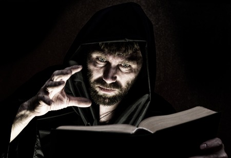 necromancer casts spells from thick ancient book by candlelight on a dark background.