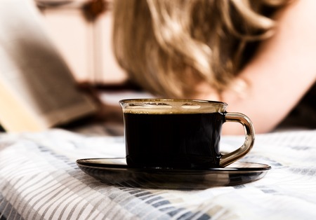 beautiful woman reading a thick book lying on the bed, close-up coffee cup.の写真素材