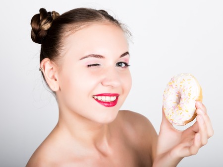 girl in bright makeup eating a tasty donut with icing. Funny joyful woman with sweets, dessert. dieting concept. junk food.の写真素材