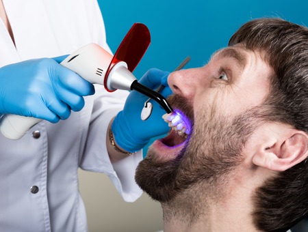 The reception was at the female dentist. Doctor examines the oral cavity on tooth decay. Caries protection. Tooth decay treatment. Dentist working with dental polymerization lamp in oral cavity.の写真素材