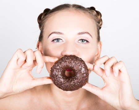 girl in bright makeup eating a tasty donut with icing. Funny joyful woman with sweets, dessert. dieting concept. junk food. girl looking through donut hole.の写真素材