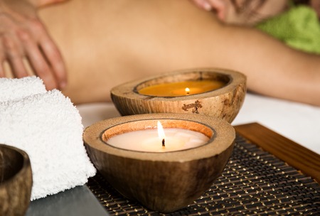 Young woman receiving a back massage in the spa salon. close-up of a candle and towels. woman with eyes closed lying on massage table at salon.の写真素材